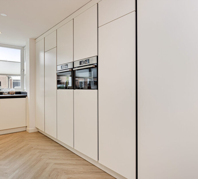 Kastenwand, moderne keuken, moderne kastenwand, keuken met kastenwand, verticale greeplijsten, zwarte verticale greeplijsten, zwarte greeplijsten, zwarte grepen, greepprofielen, twee ovens, kastenwand met ovens, zijdeglans lak fronten, witte keuken.