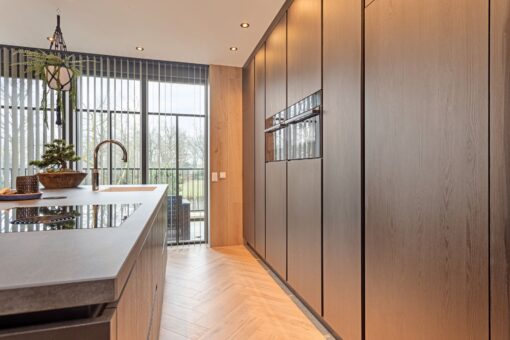 Moderne keuken Someren, keukenstudio Someren, keuken op maat someren, Keramisch werkblad, Kookeiland, kastenwand, , Geïntegreerde Bora kookplaat met afzuiging, Franke Fragranite witte vlakinbouw spoelbak, Quooker kraan Flex chroom, Zwart houtdecor fronten, Zwarte horizontale en verticale greeplijsten.
